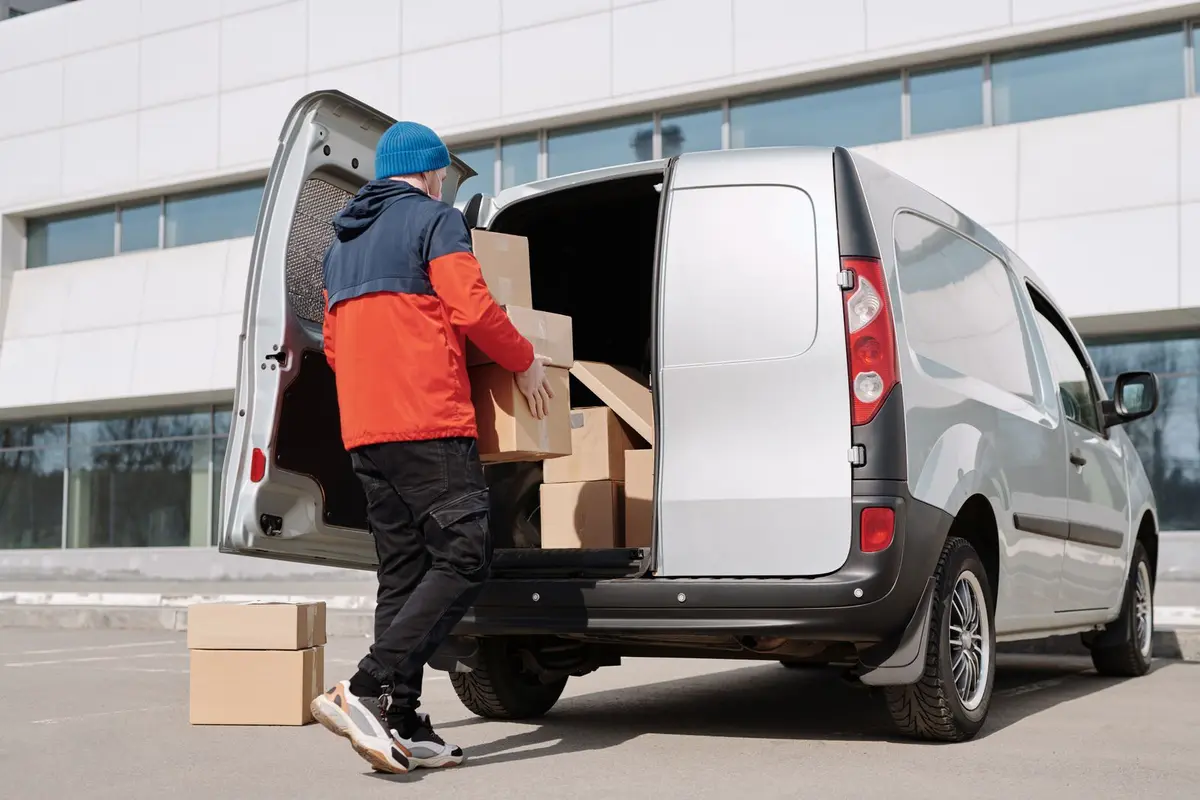 Livreur chargeant des cartons dans un véhicule utilitaire devant un entrepôt
