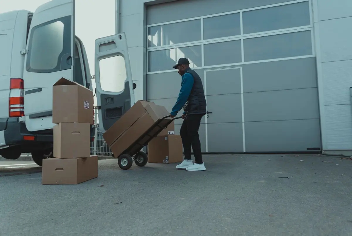 Livreur déplaçant des cartons sur un diable devant un utilitaire